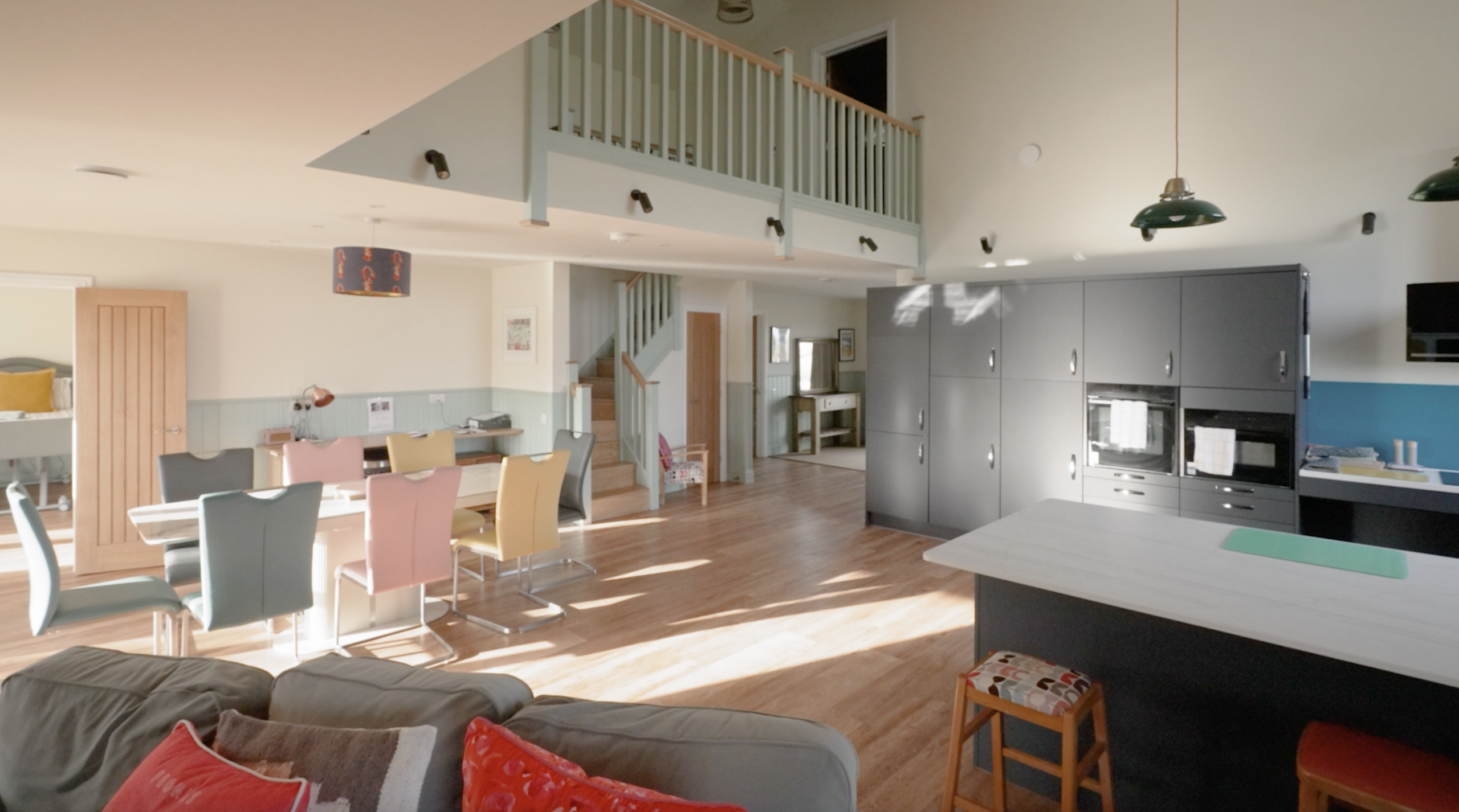 Spacious, open-plan adapted home interior with abundant natural light, featuring a kitchen, dining area, and accessible layout with wide walkways, soft-toned finishes, and a mezzanine level above.
